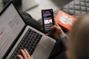 person looking at phone and typing on computer 